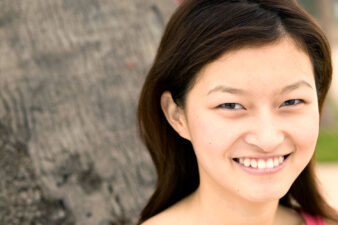Natural outdoor headshot of a young Asian actress smiling with a relaxed, engaging expression, from Ken Weingart's actor headshot portfolio.